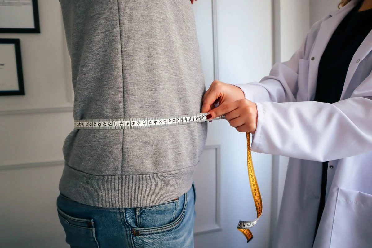 Medição de circunferência abdominal durante uma avaliação clínica, sem rostos visíveis.