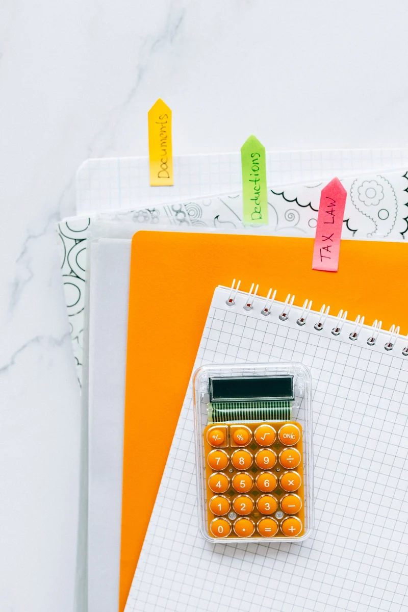 Calculadora, caderno e documentos organizados sobre uma mesa.
